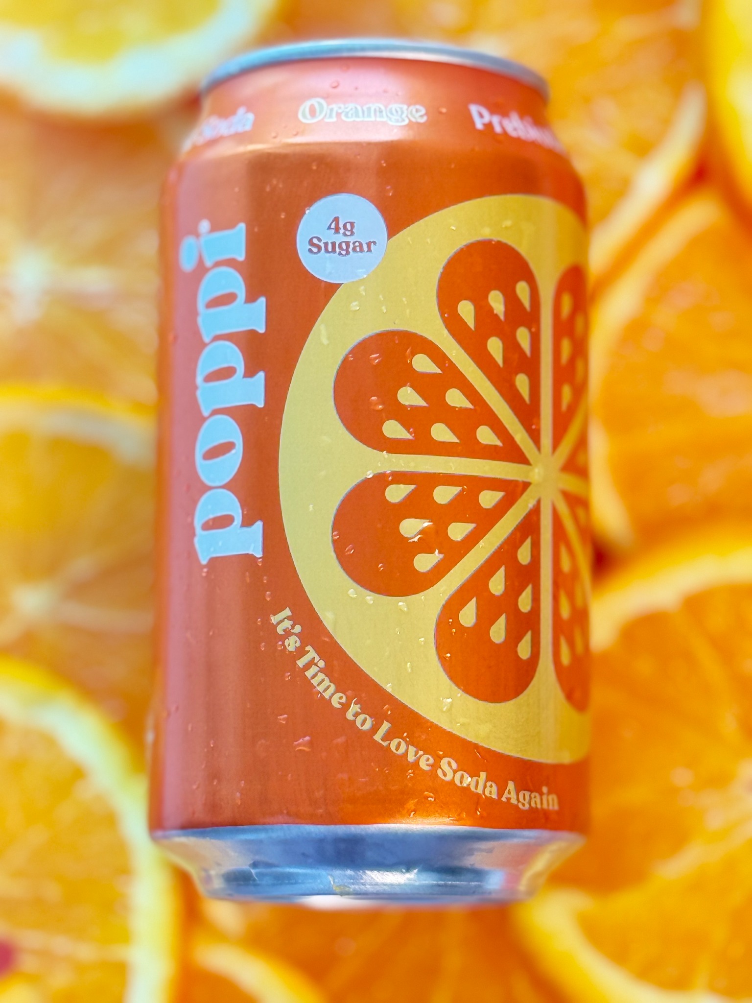 An Orange Poppi prebiotic soda can styled against sliced oranges.