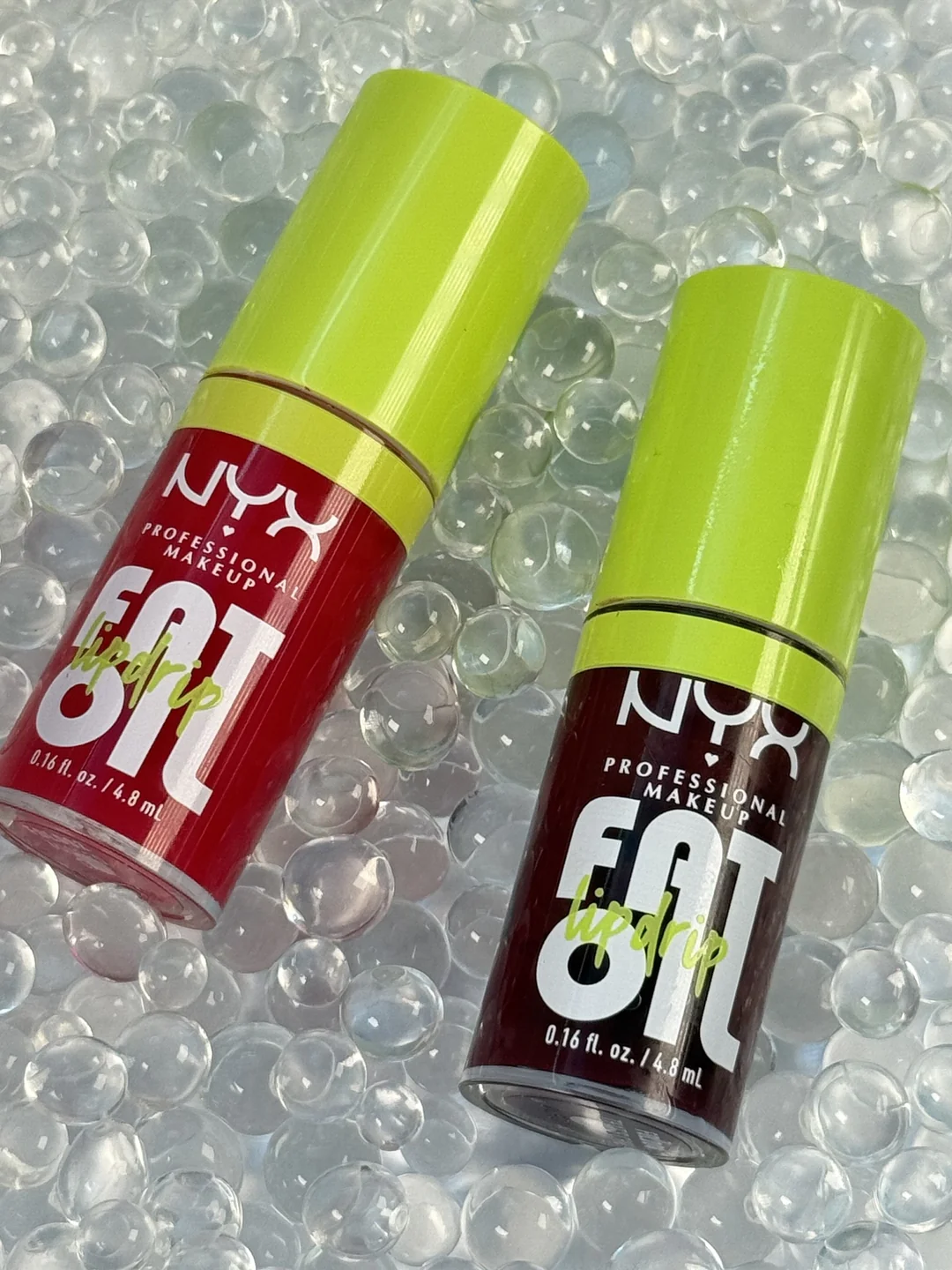 Two NYX Fat Oil Lip Drip makeup bottles with chartreuse caps styled on clear water beads.