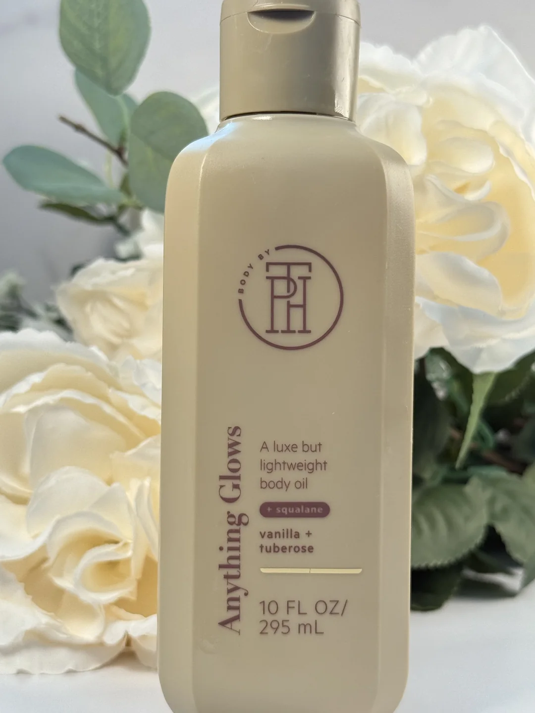Body By PH Anything Glows vanilla and tuberose body oil among creamy white rose blooms.